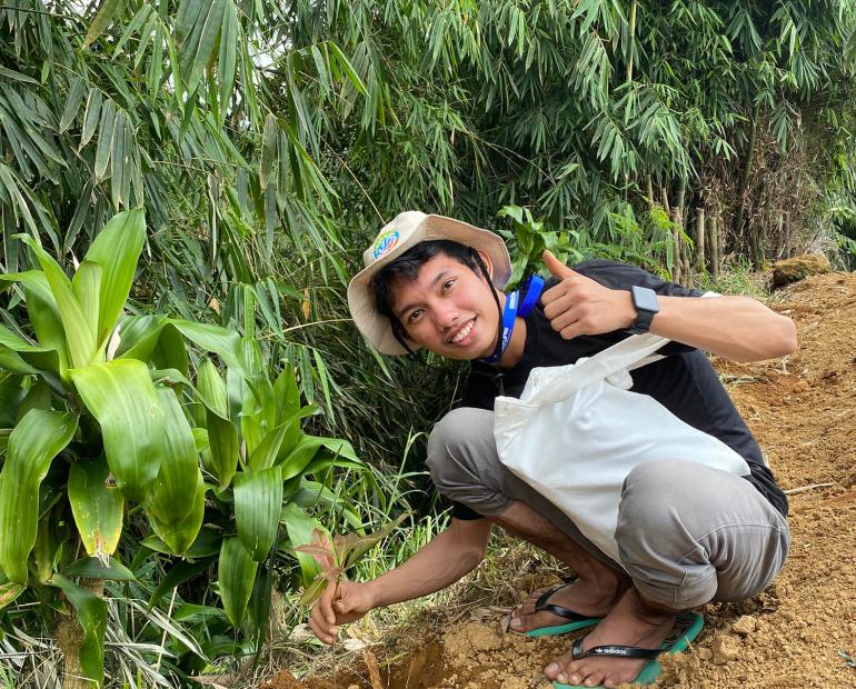 A young person sitting on the ground next to trees